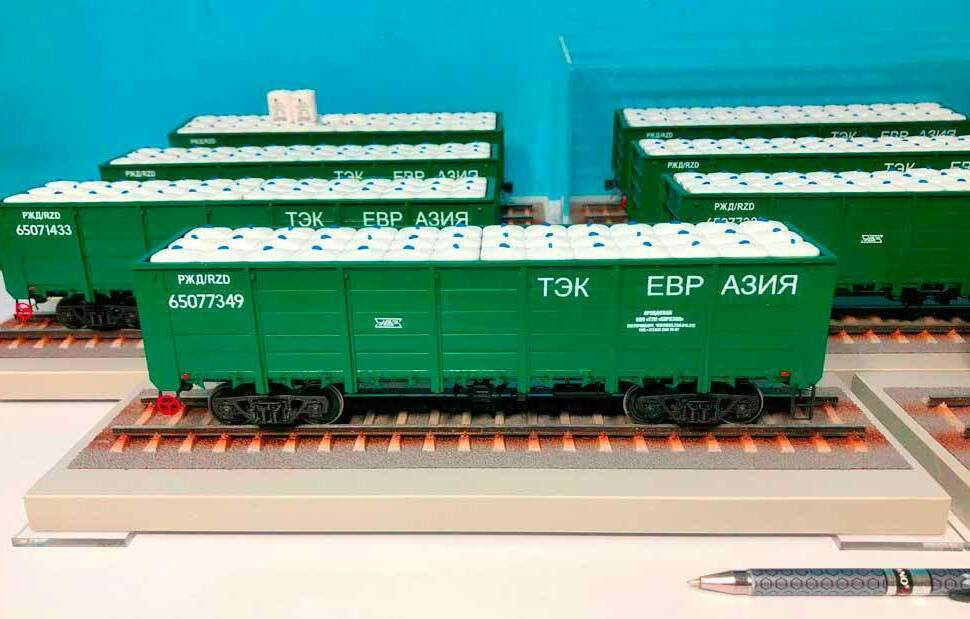 Макет зелёного грузового вагона «ТЭК ЕВР АЗИЯ» на железнодорожных путях Масштабная модель зелёного железнодорожного полувагона РЖД с логотипом «ТЭК ЕВР АЗИЯ», загруженного белыми контейнерами, на демонстрационном стенде