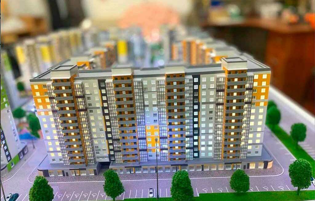 Архитектурный макет современного жилого комплекса с парковкой и озеленением Детальный масштабный макет многоквартирного жилого дома: высокий жилой комплекс с балконами, витражным остеклением, парковкой и деревьями по периметру