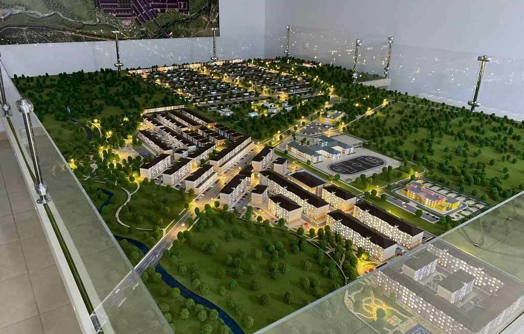 Архитектурный макет микрорайона и коттеджного посёлка, выполненный на заказ для выставки Детализированный архитектурный макет современного жилого комплекса с подсветкой: кварталы малоэтажных домов, школа, спортплощадки и парковые зоны в окружении леса, выполненный на заказ для выставки