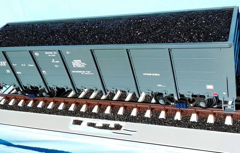 Детализированный макет грузового железнодорожного вагона с углем на рельсах Модель открытого грузового железнодорожного вагона с угольной загрузкой, установленного на участке железнодорожного пути, вид сбоку