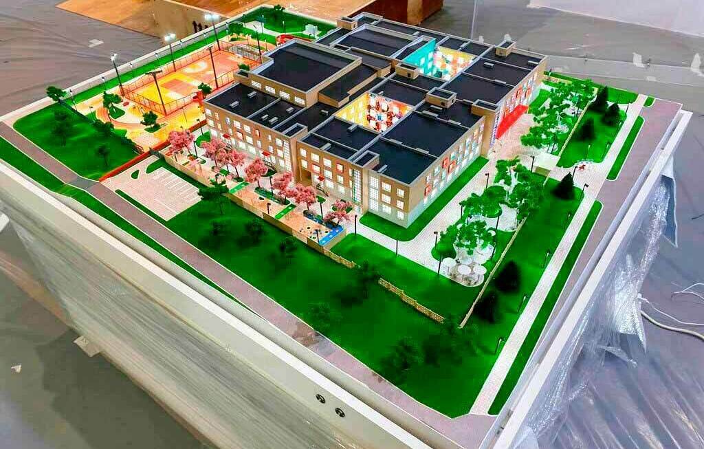 Архитектурный макет школы / современного учебного комплекса с подсветкой и благоустройством территории Детализированный архитектурный макет школьного кампуса с основным корпусом, зелёными зонами, спортивной площадкой и парковкой, выполненный с интерьерной и ландшафтной подсветкой