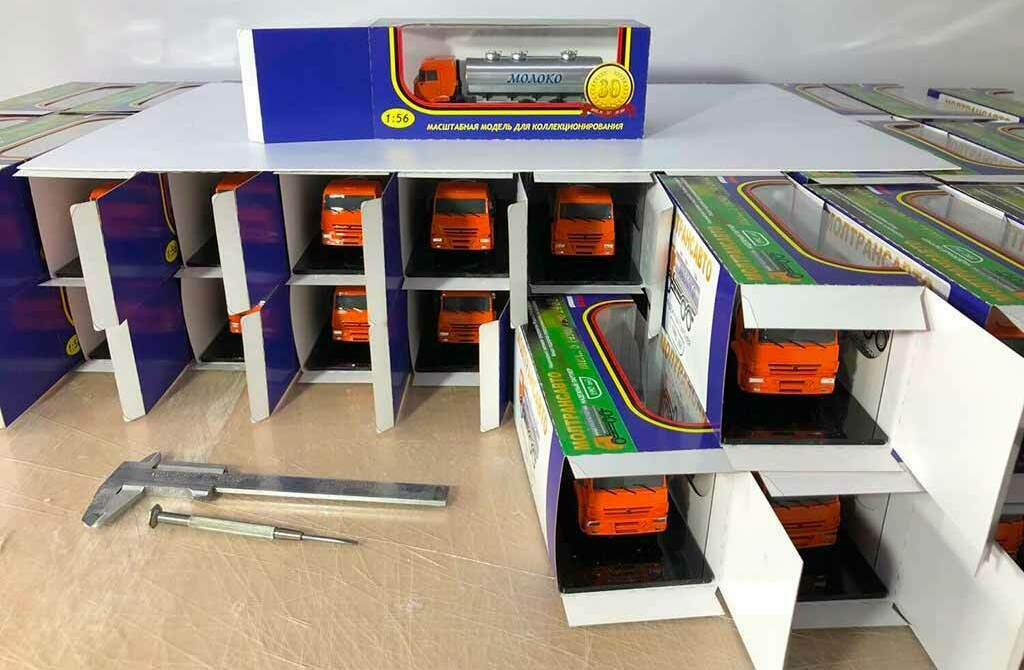 Масштабные модели грузовиков 1:43 в фирменной упаковке – проверка и разработка макета коробки Ряд оранжевых масштабных моделей грузовиков 1:43 в картонных коробках, процесс разработки и измерения макета упаковки штангенциркулем. Модели камазов в упаковках - подарочных коробках