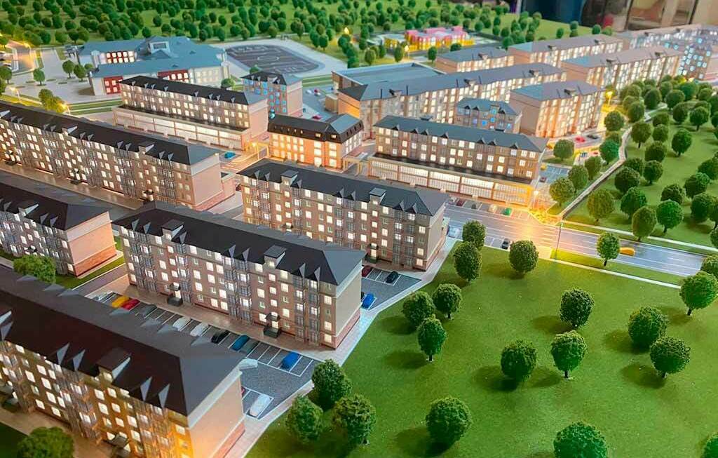 Архитектурный макет современного жилого комплекса с озеленением и подсветкой Детализированный архитектурный макет жилого квартала: многоэтажные дома, дороги, парковки и зелёная парковая зона с деревьями