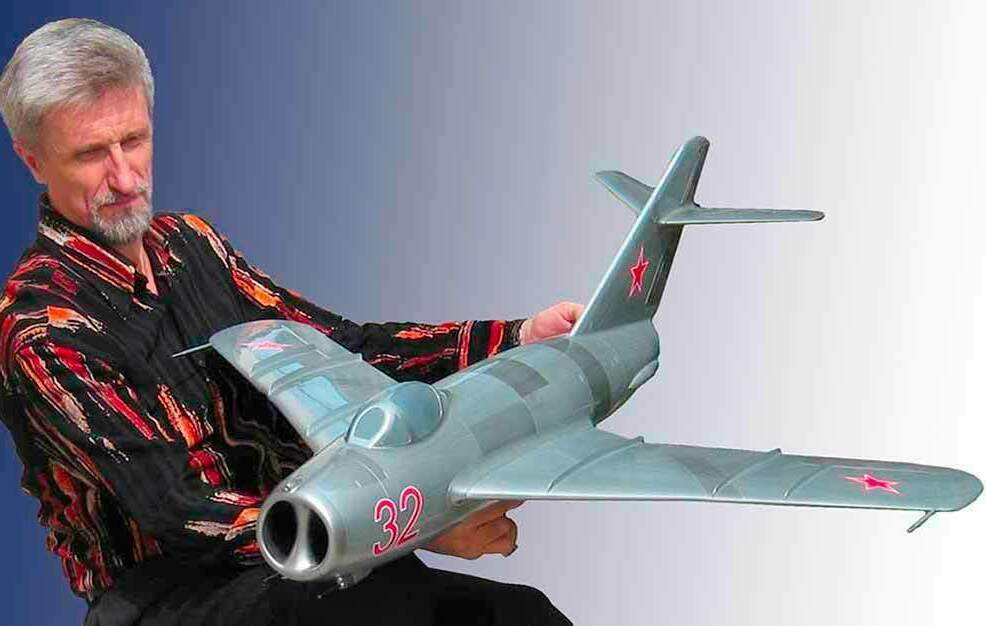Масштабный макет самолёта на заказ. Модель реактивного самолёта МиГ‑15 Масштабный макет самолёта на заказ изготовленный для подарка. Мужчина держит крупную модель реактивного самолёта МиГ‑15 с красными звёздами и номером 32, вид сбоку