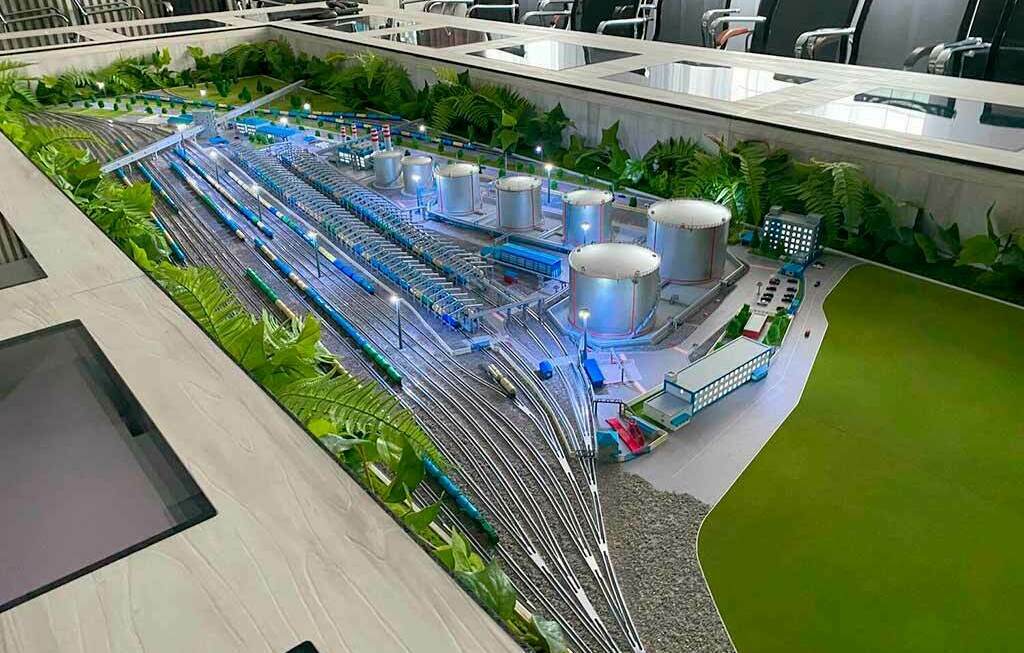 Интерактивный макет нефтебазы с железнодорожной станцией, встроенный в стол переговорной комнаты Интерактивный световой макет промышленной нефтебазы с резервуарами и железнодорожными путями, размещённый в центре стола переговорной комнаты, изготовленный для выставки.